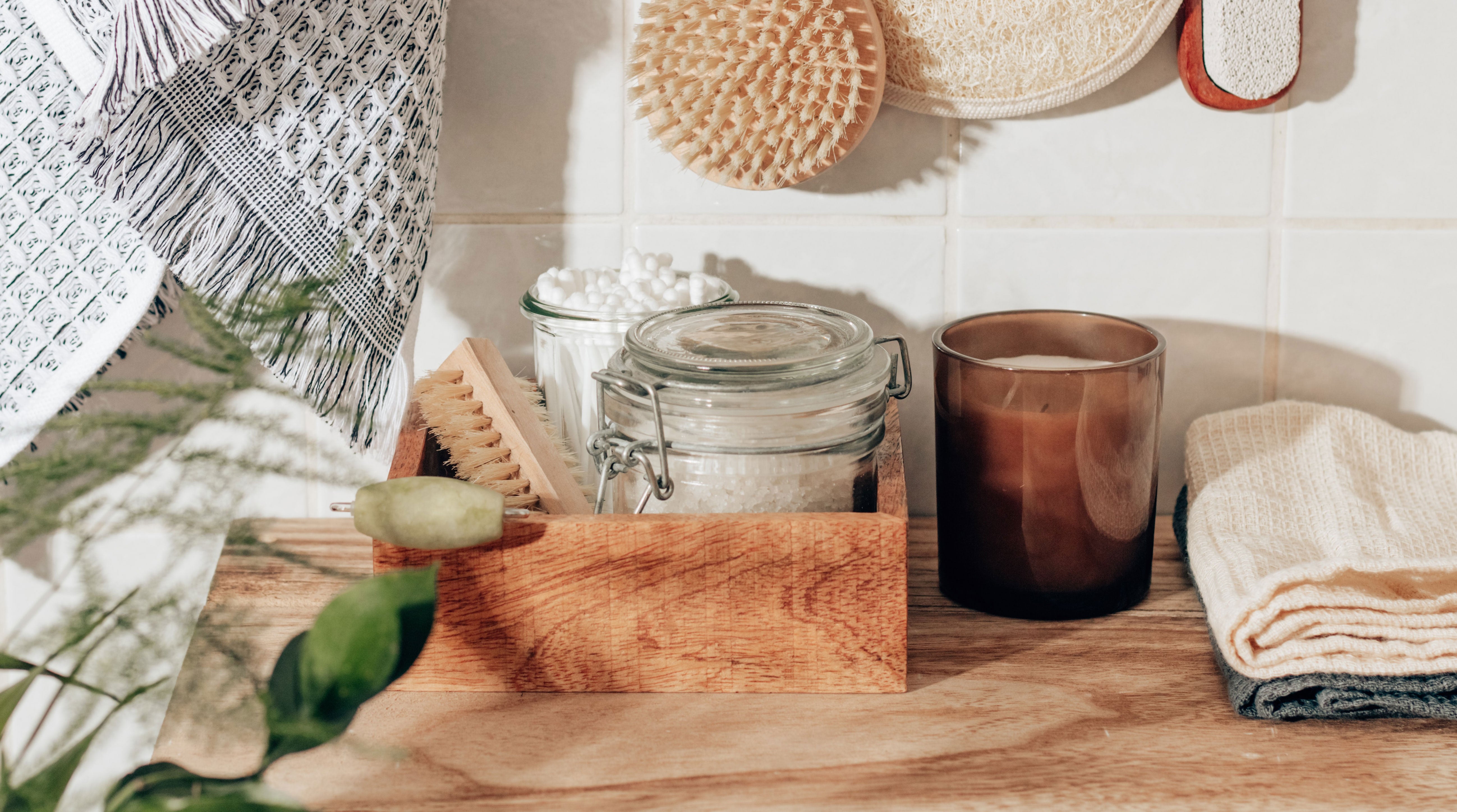 Natural bathroom products on a shelf including soap, candle, and washcloths. 