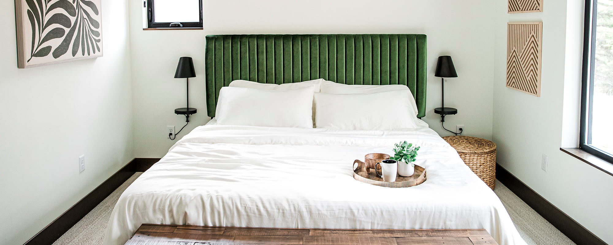 Bed covered in natural white YALA Luxe Sateen bamboo bedding. with a green velevet headboard and a tray on the bed with coffee on it.