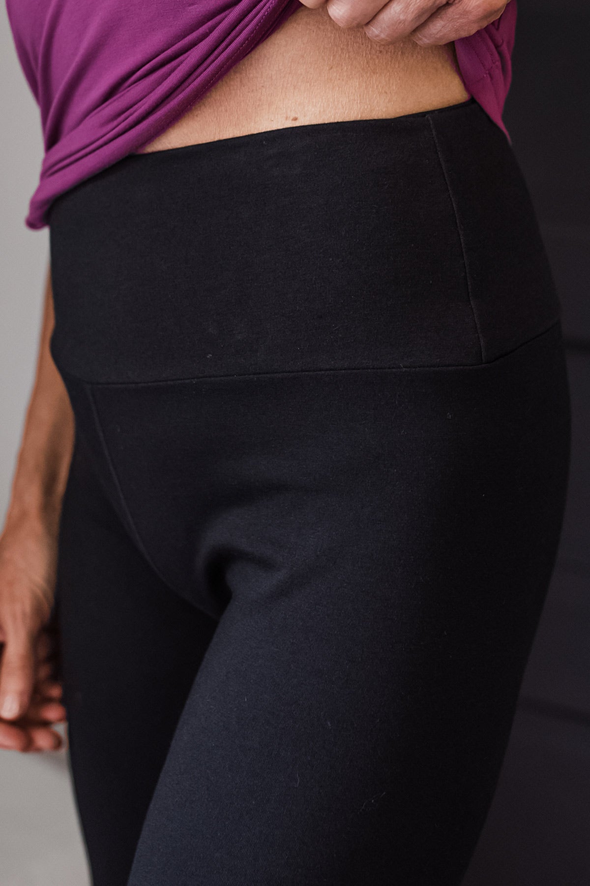 Close shot of a woman's waist and hips, shirt slightly raised to show off the waistband, wearing Yala Ashlyn Ultra-Stretch Bamboo & Organic Cotton Bootcut Legging in Black