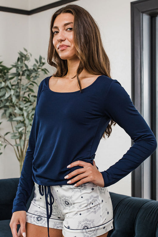 A woman standing facing slightly to the side with one hand on her hip, wearing Yala Avril Scoop Neck Long Sleeve Bamboo Top in Navy