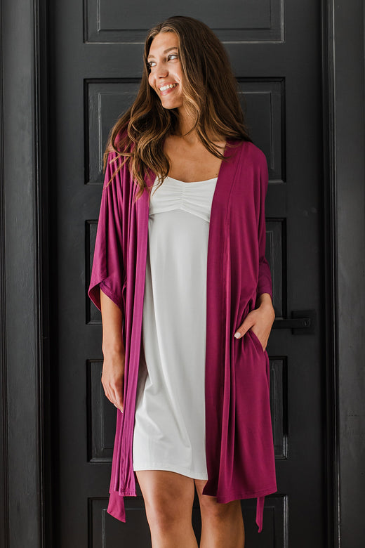 A woman standing in front of a closed door, smiling and looking off to the side, wearing Yala Cleo Babydoll Bamboo Nightgown in Natural