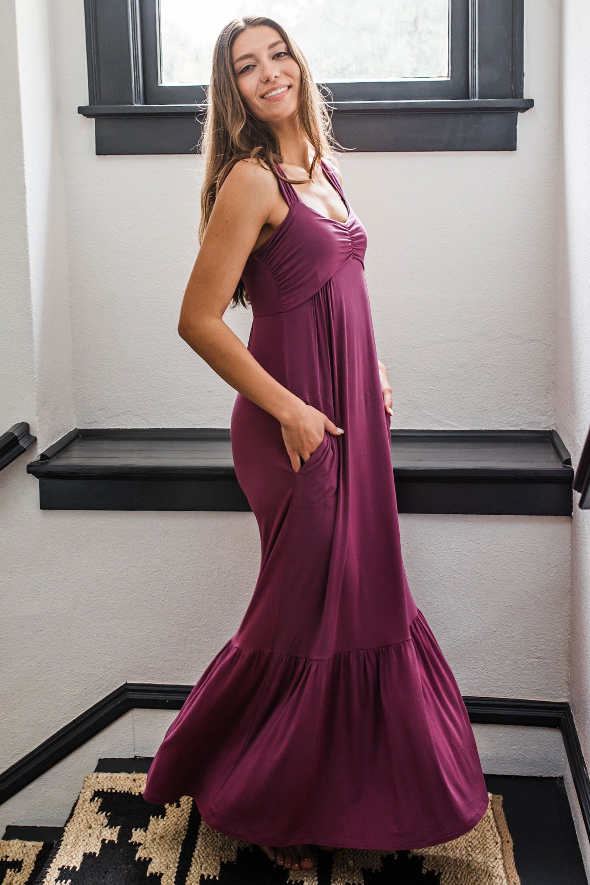 A womand standing facing sideways while looking at the camera with her hands in her pockets, wearing Yala Cleo Bamboo Babydoll Maxi Dress in Boysenberry
