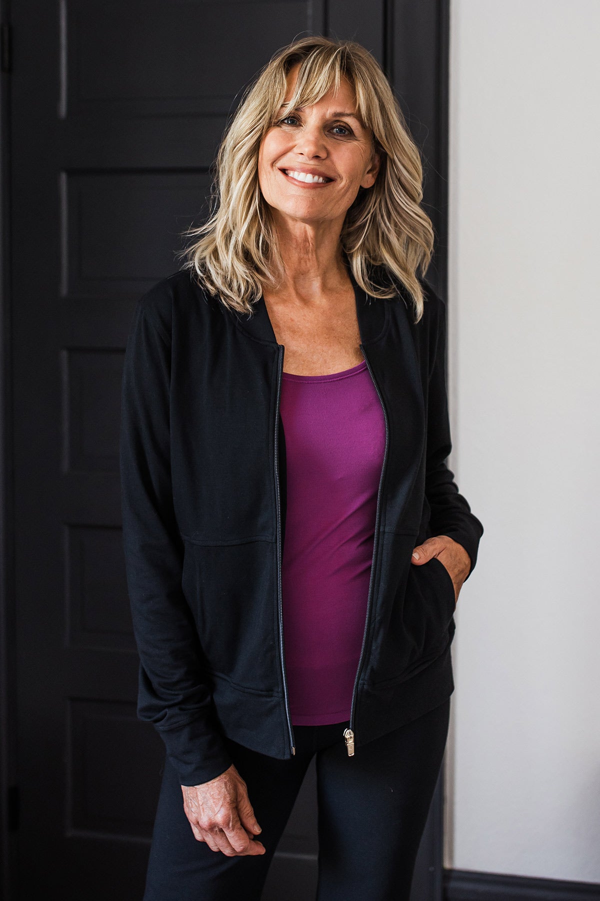 A woman standing with one hand in her pocket and a smile on her face, wearing Yala Danielle Ultra-Stretch Bamboo & Organic Cotton Track Jacket in Black