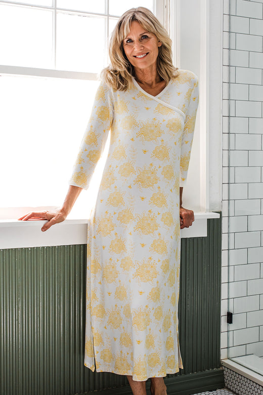 A woman leaning back against a window sill and smiling, wearing Yala Haley Crossover Front 3/4 Sleeve Bamboo Nightgown in Honeybee Print