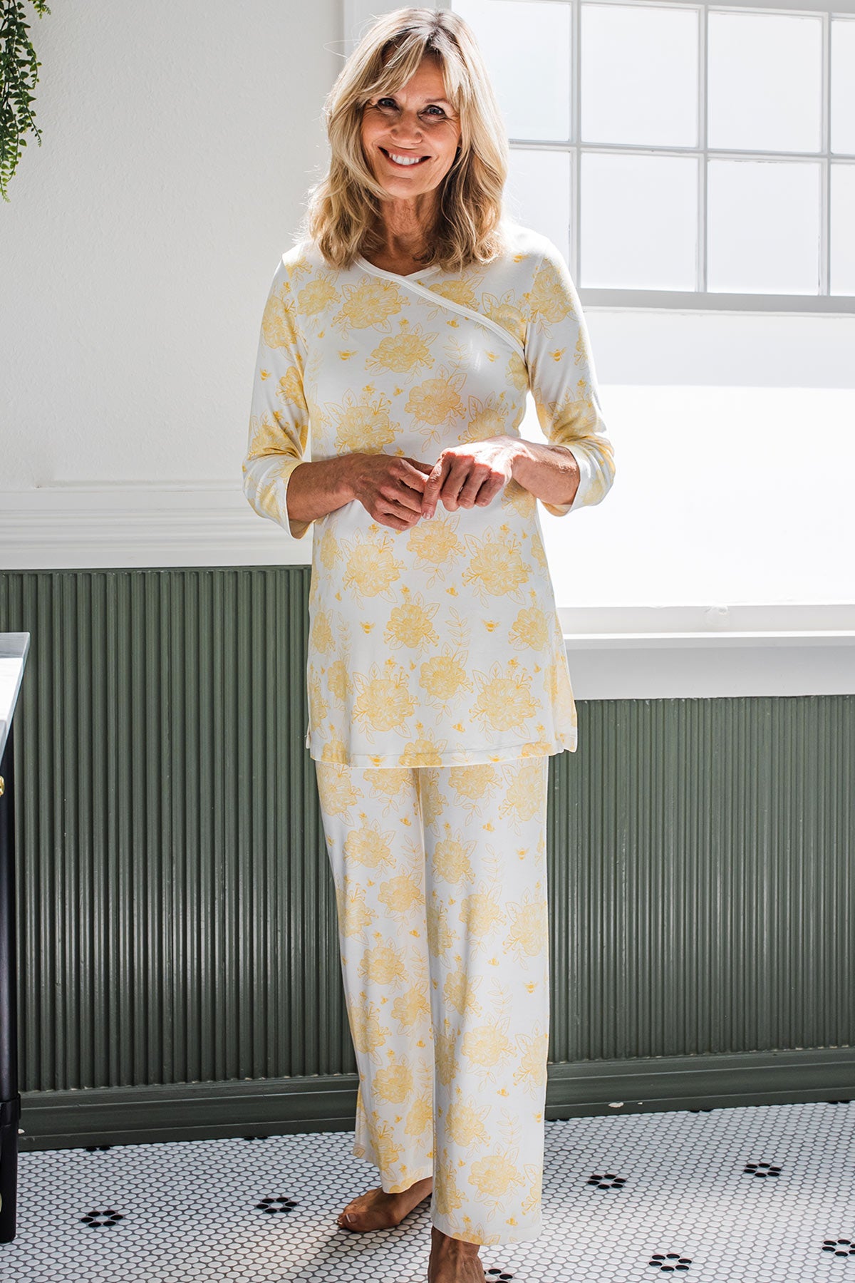 A woman standing with her hands in front of her and smiling, wearing Yala Crossover Front 3/4 Sleeve Bamboo Pajama Set in Honeybee Print