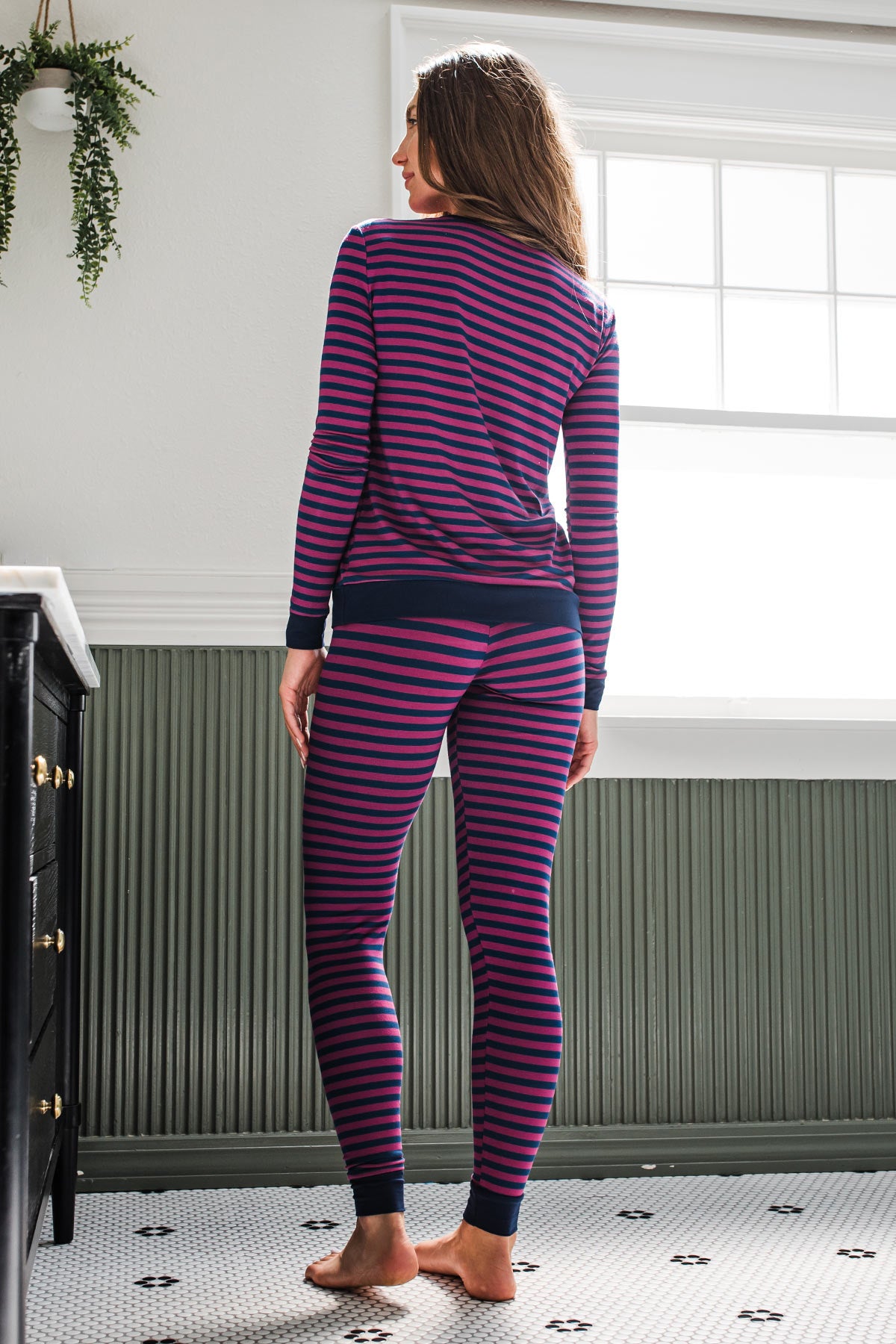A woman standing facing away from the camera with her hands at her sides, looking off to the side, wearing Yala Lola Striped Bamboo Pajama Set in Berry Classic Stripe