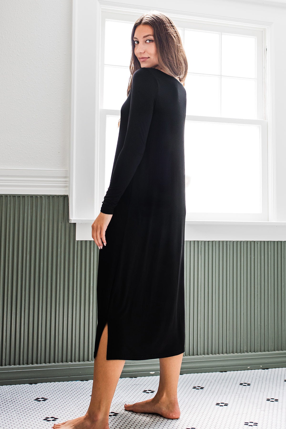 A woman standing with her back to the camera, head turned to look back, wearing Yala Scoop Neck Long Sleeve Bamboo Nightgown in Black