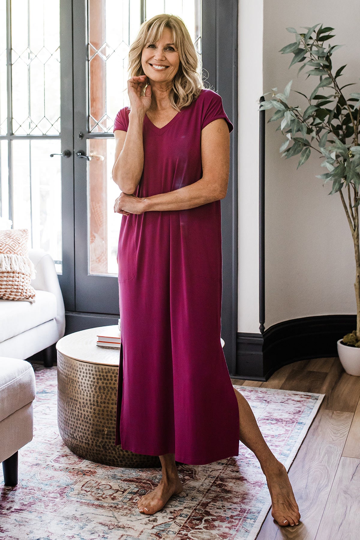 A woman standing and smiling with one foot stretched out to the side, wearing Yala Sloane V-Neck Cap Sleeve Bamboo Maxi Dress in Boysenberry