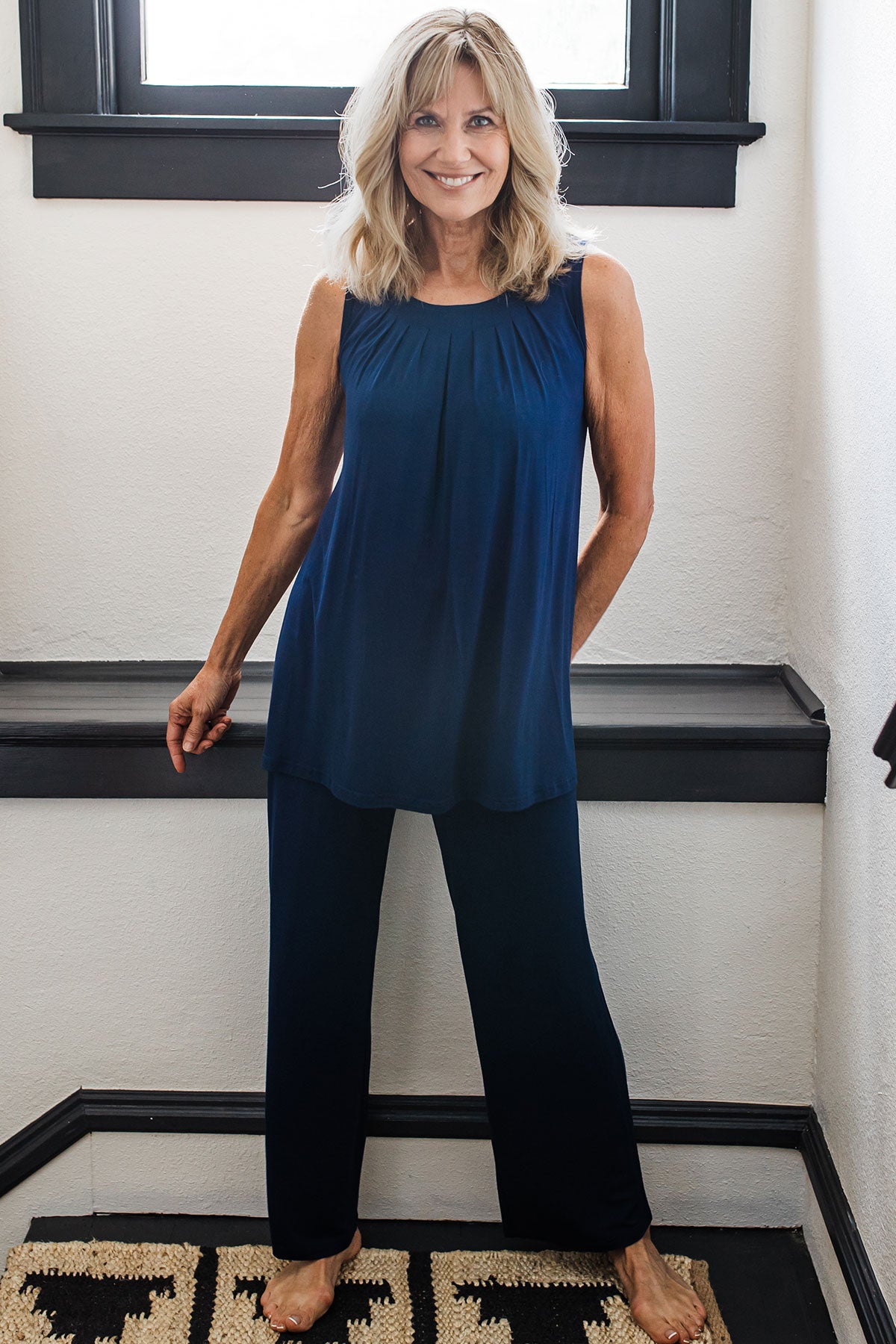 A woman standing in front of a hallway ledge, wearing Yala Delia Gathered Tank Bamboo Pajama Set in Navy