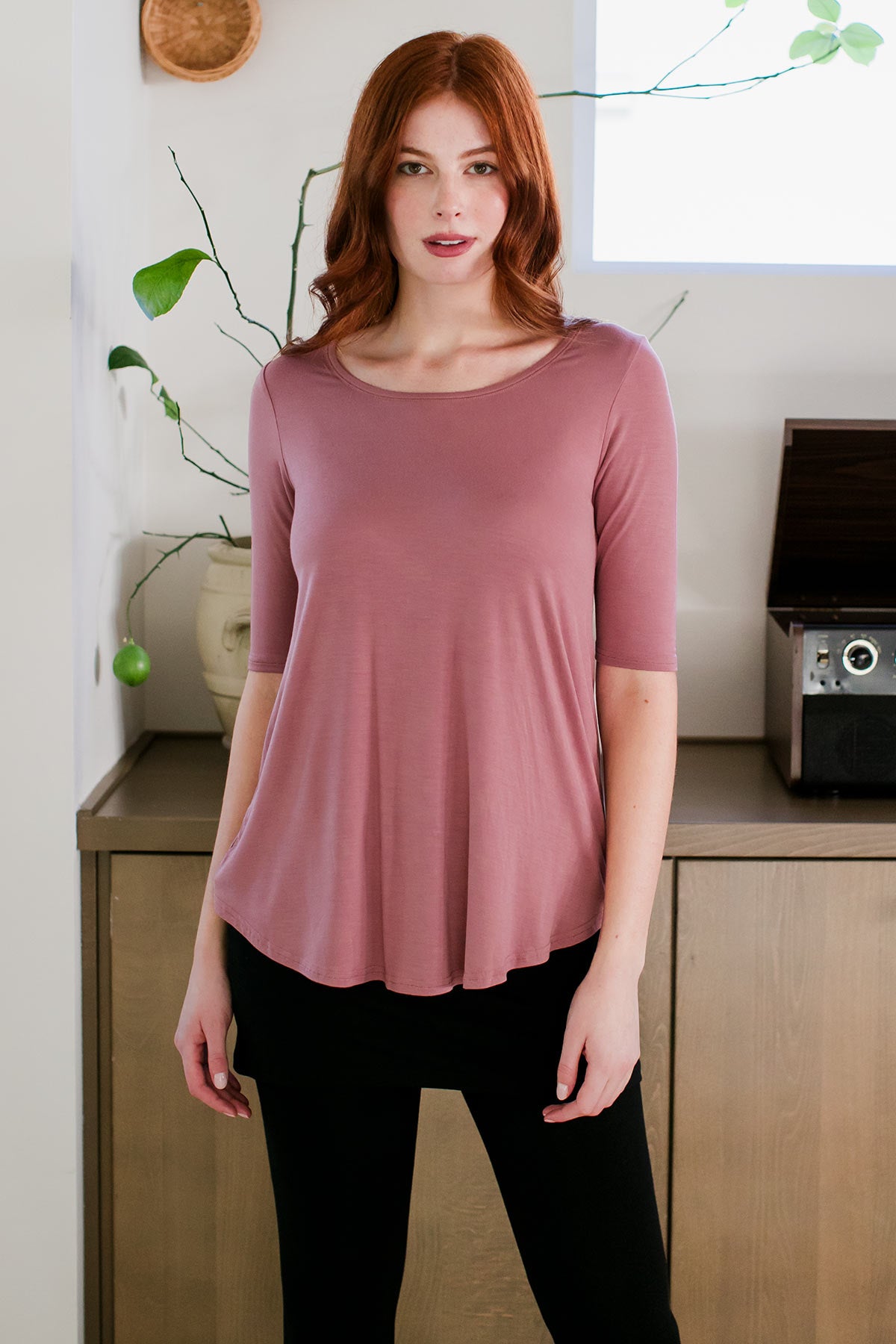 A woman standing with haer hands at her sides, wearing Yala Sandy Relaxed Fit Scoop Neck Short Sleeve Bamboo Top in Rose