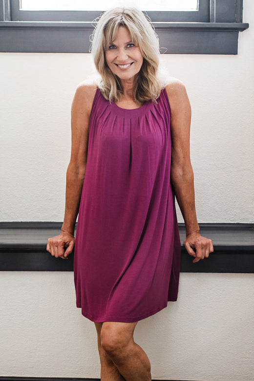 A woman standing leaned back against a ledge with a smile on her face, wearing Yala Delia Gathered Tank Bamboo Nightgown in Boysenberry