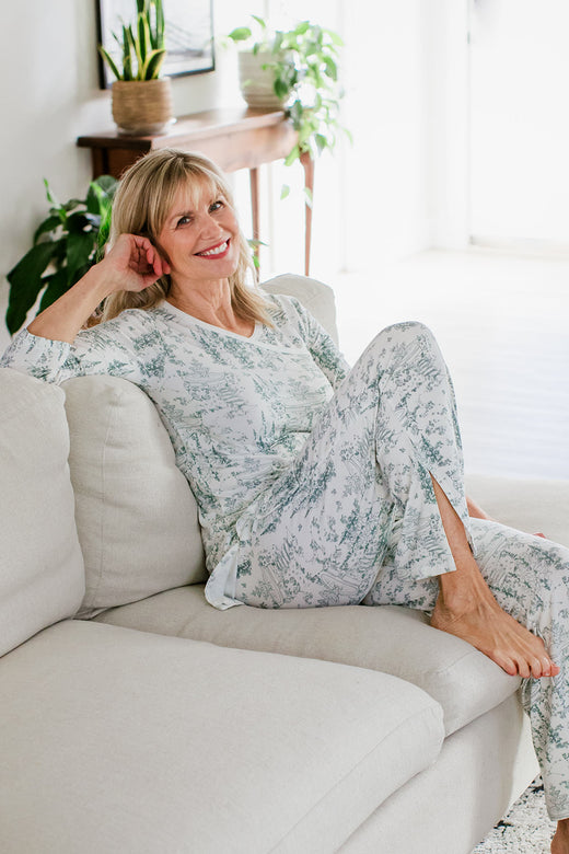 A woman sitting on a couch, one hand held beside her head, wearing Yala Haley Crossover Front 3/4 Sleeve Bamboo Pajama Set in English Garden Print