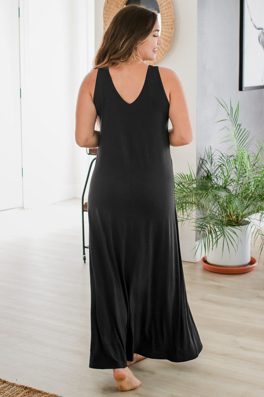 A woman walking away from the camera with her hands held in front of her, wearing Yala Kinsley Sleeveless Bamboo Maxi Dress in Black