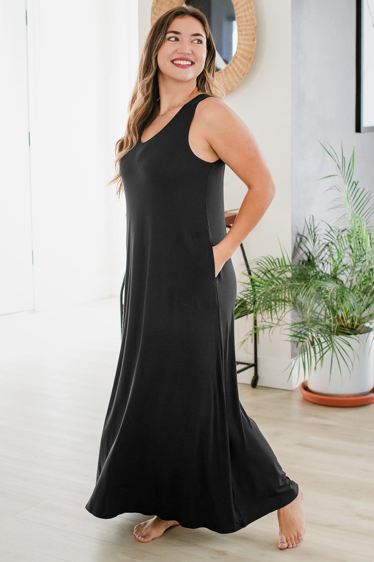 A woman standing facing to the side, one foot extended behind her and her head turned to look behind, wearing Yala Kinsley Sleeveless Bamboo Maxi Dress in Black
