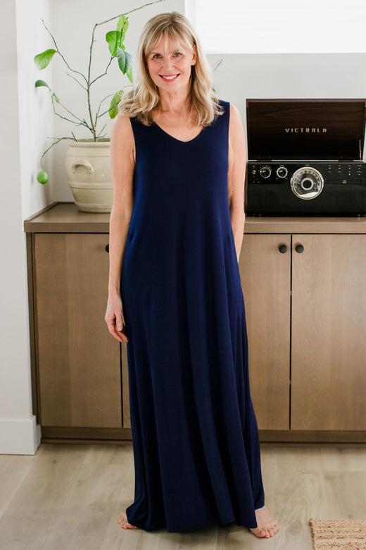 A woman standing with a smile on her face and one arm behind her back, wearing Yala Kinsley Sleeveless Bamboo Maxi Dress in Navy