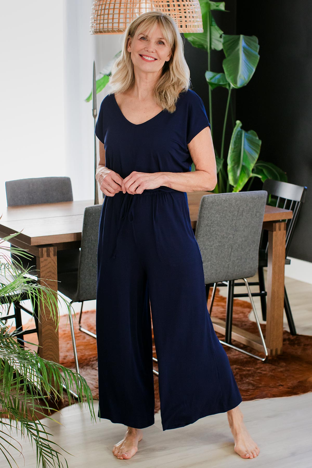 A woman standing with a wide stance, her hands held in front of her waist, wearing Yala Kiova V-Neck Bamboo Jumpsuit in Navy