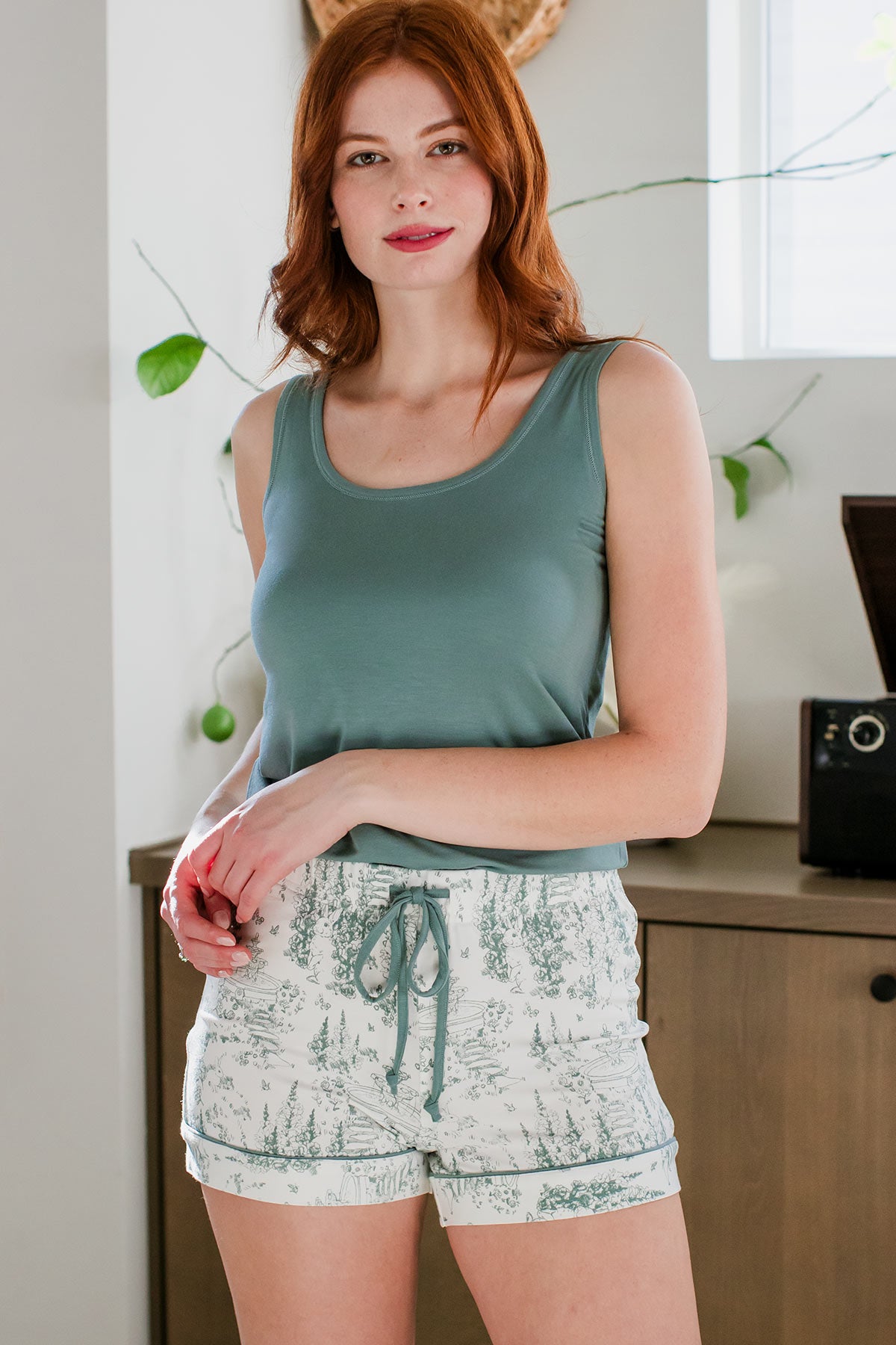 A woman standing with her hands held together resting on her hip, wearing Yala Lauren Piped Bamboo Pajama Shorts in English Garden Print
