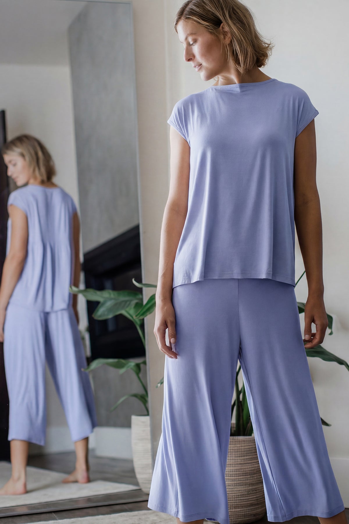 Woman wearing a light purple outfit standing in a room with a mirror.
