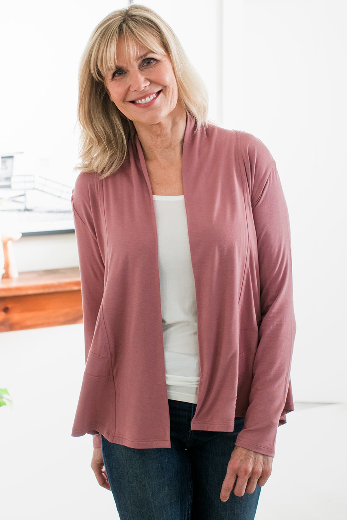 A woman standing with her head tiled to the side and a smile on her face, wearing Yala Tatum Hi-Low Bamboo Cardigan Wrap in Rose