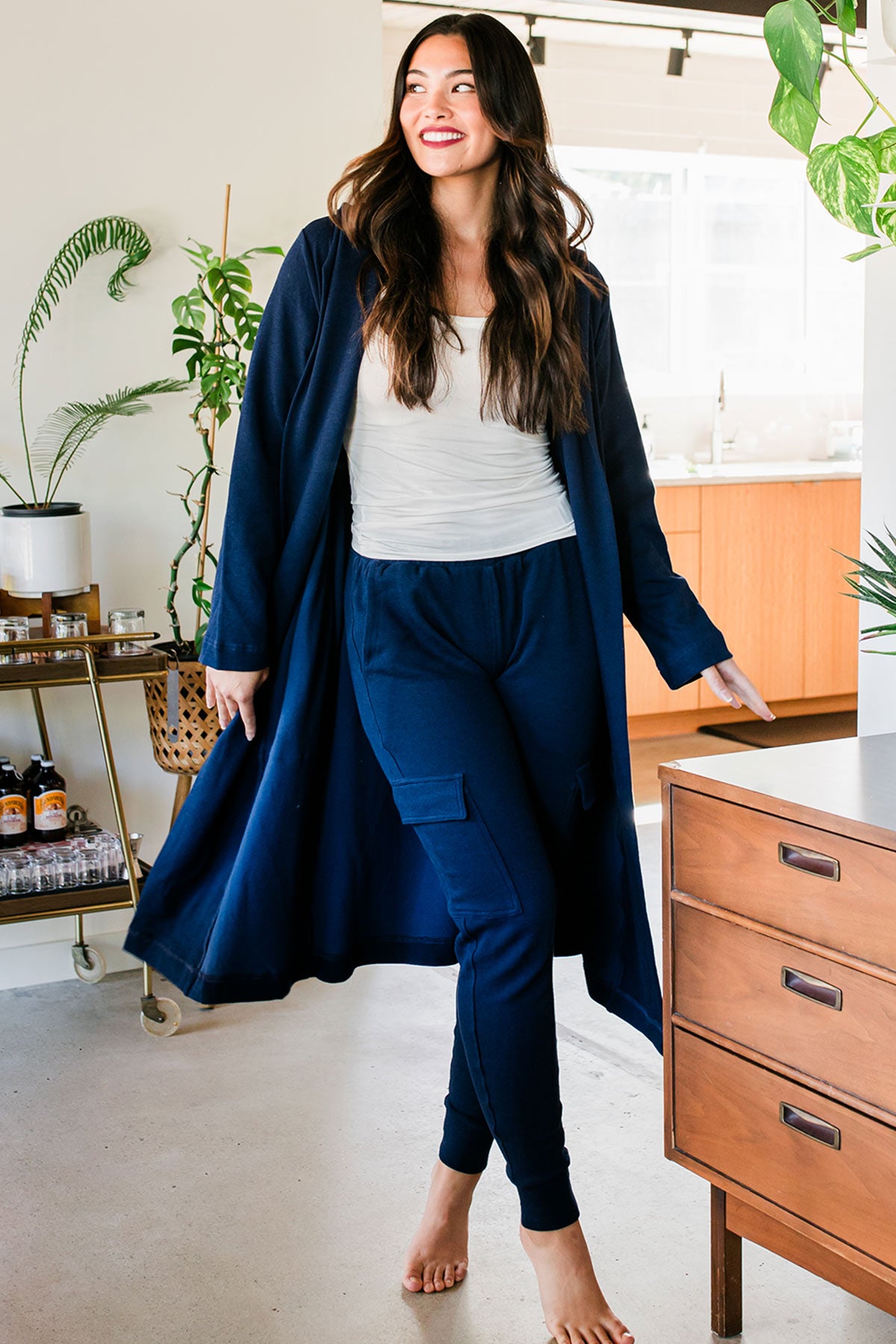 A woman stepping forward with one leg crossing in front of the other, wearing Yala Elliot Bamboo & Organic Cotton Sweatshirt Hooded Robe in Navy