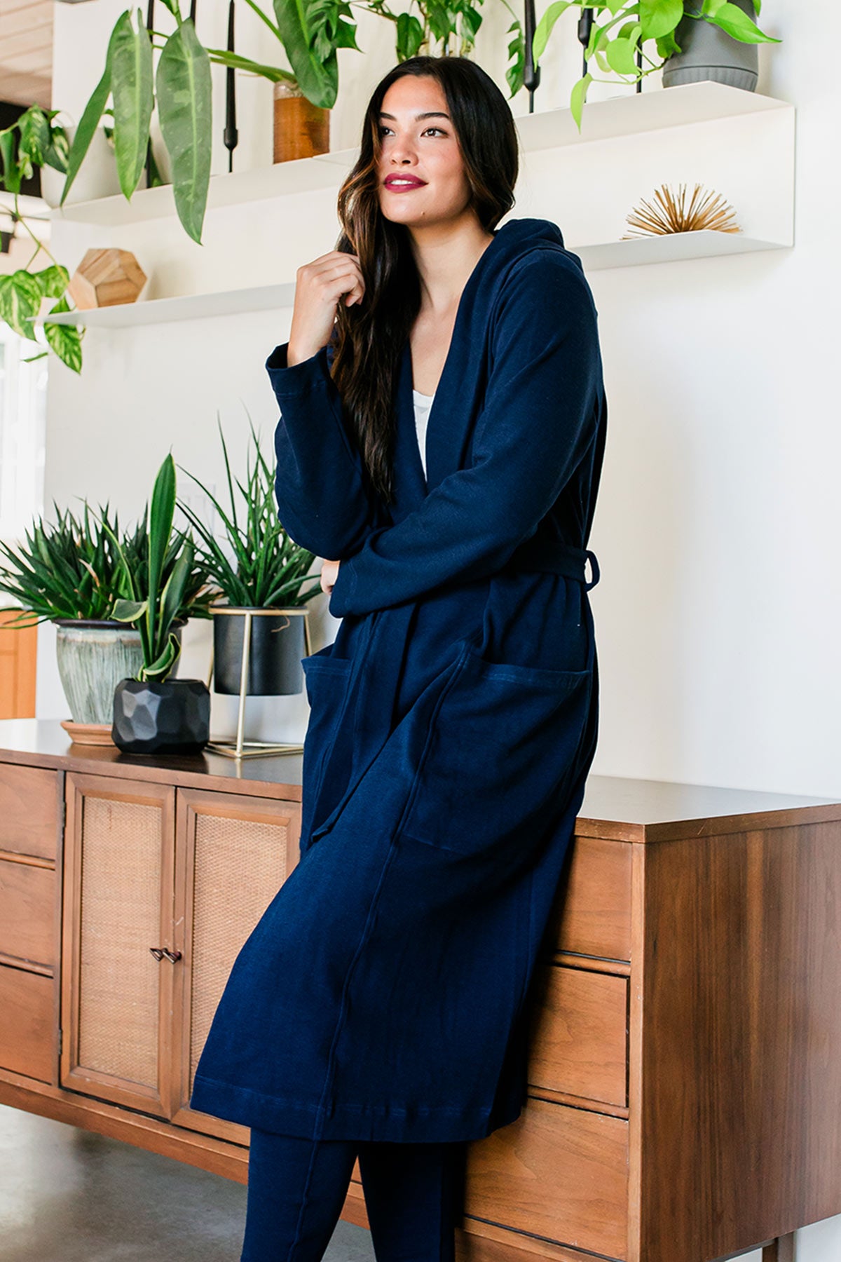 A woman standing and leaning back against a countertop, wearing Yala Elliot Bamboo & Organic Cotton Sweatshirt Hooded Robe in Navy