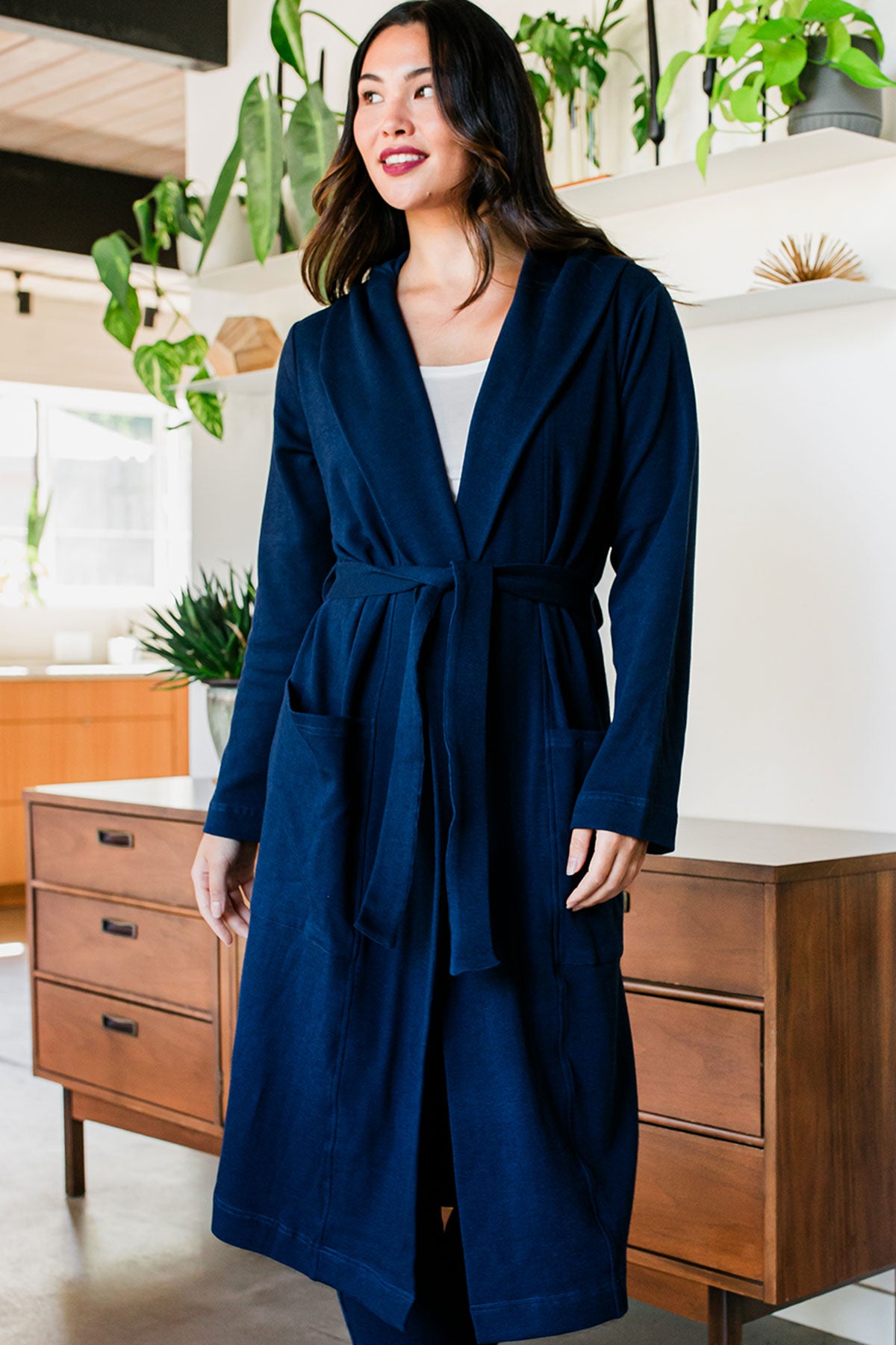 A woman standing with both hands at her sides, smiling and looking off to the side, wearing Yala Elliot Bamboo & Organic Cotton Sweatshirt Hooded Robe in Navy
