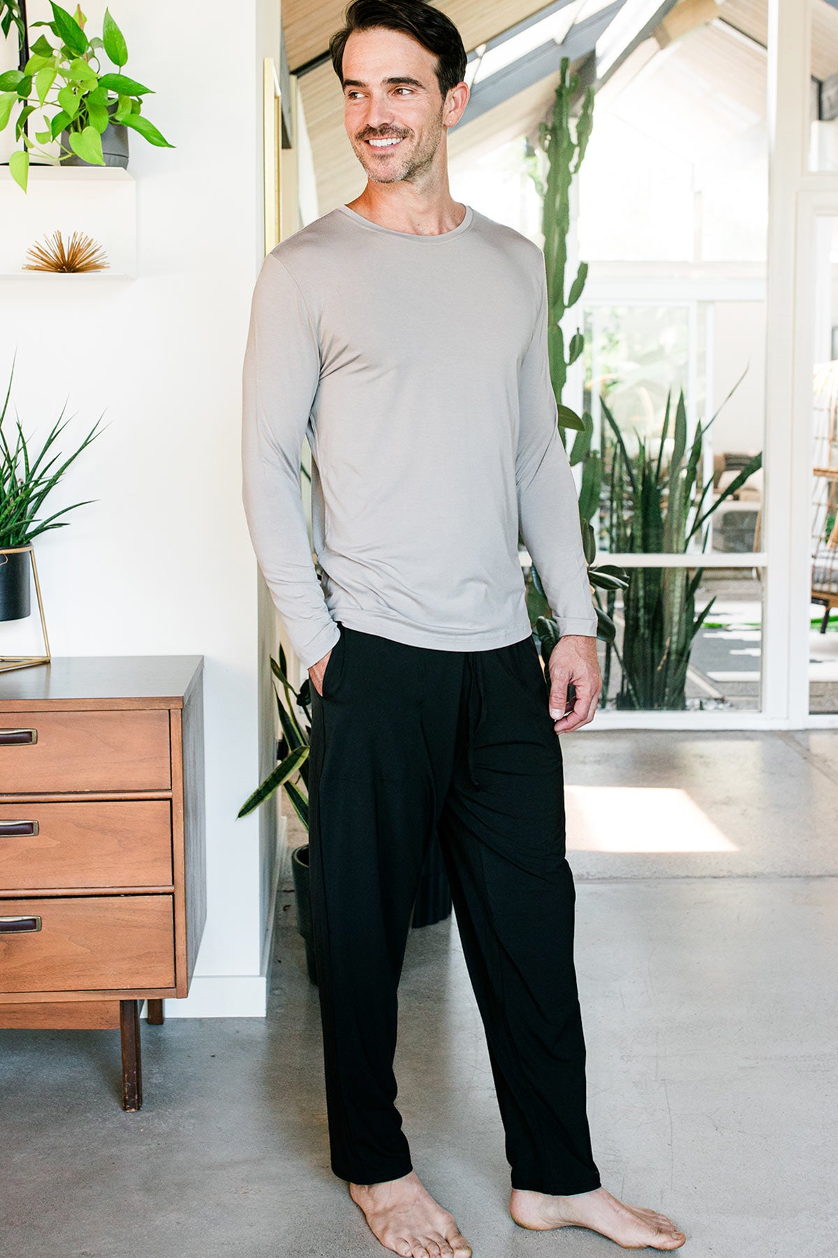 A man standing and smiling with one hand in his pocket, wearing Yala Men's Hayden ButterSoft Bamboo Lounge Pants in Black