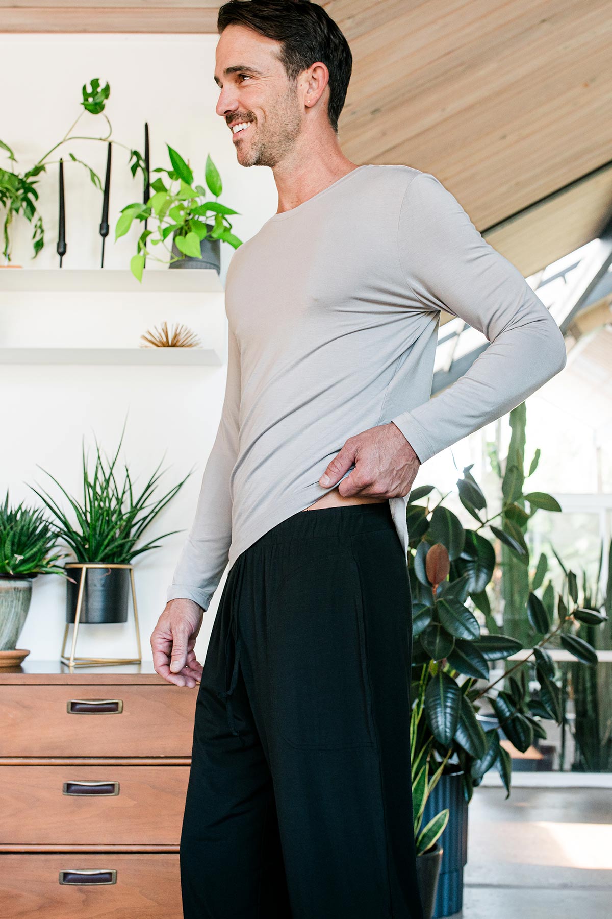 A mand standing and adjusting his shirt's hem, wearing Yala Men's Hayden ButterSoft Bamboo Lounge Pants in Black