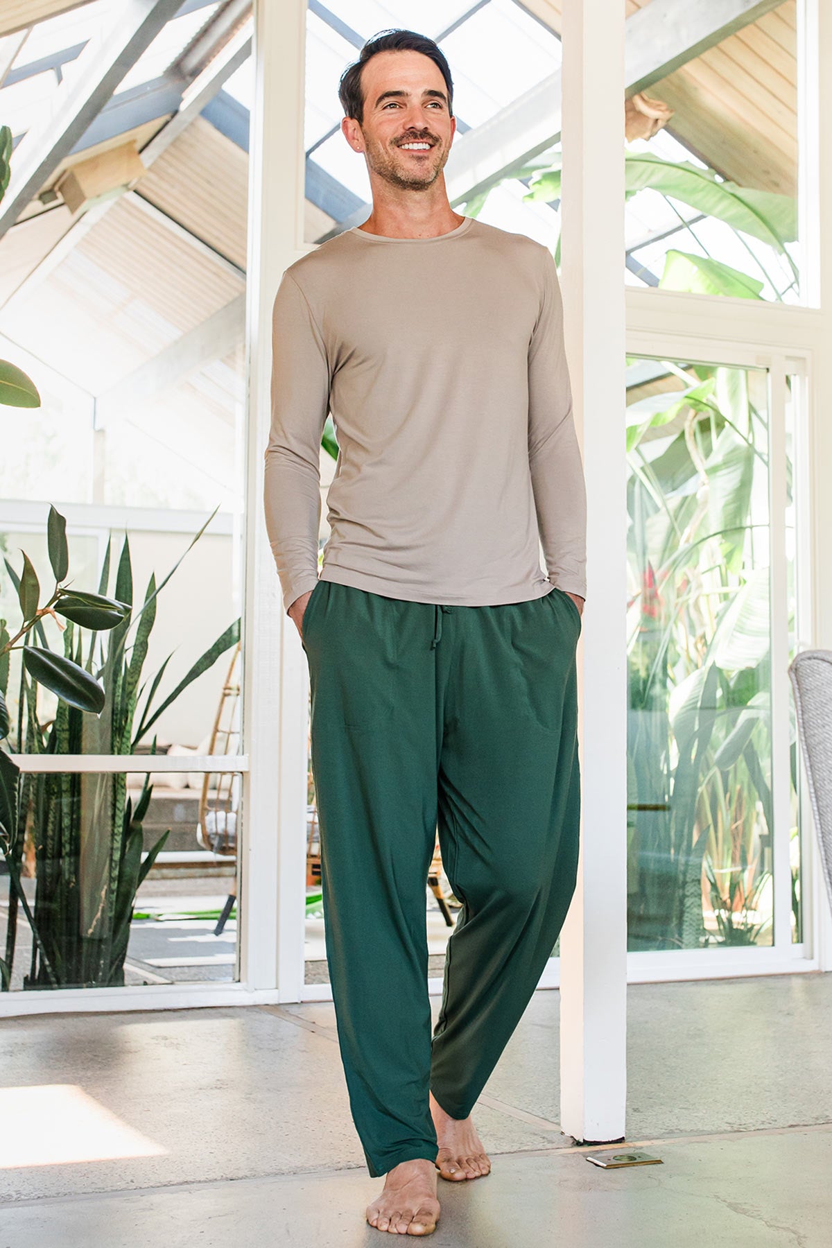 A man walking forward with both hands in his pockets and a smile on his face, wearing Yala Men's Hayden ButterSoft Bamboo Lounge Pants in Evergreem