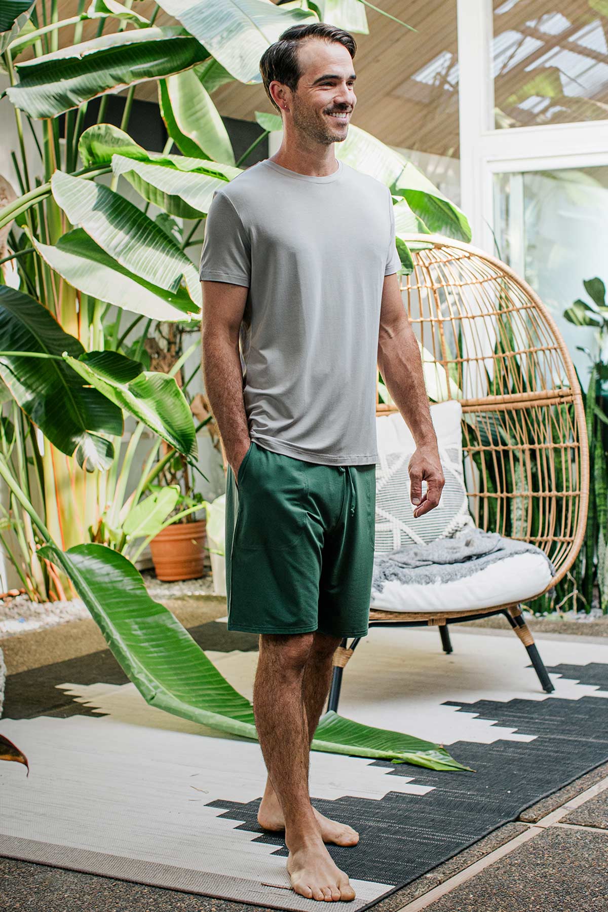 A man standing facing slightly to the side and smiling with a hand in his pocket, wearing Yala Men's Mateo ButterSoft Bamboo Lounge Shorts in Evergreen