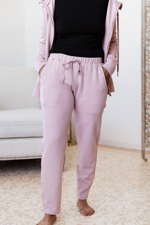 A headless shot of a woman standing with one foot forward and both hands in her pockets, wearing Yala Angel Bamboo and Organic Cotton Jogger Sweatshirt Lounge Pants in Lotus Pink