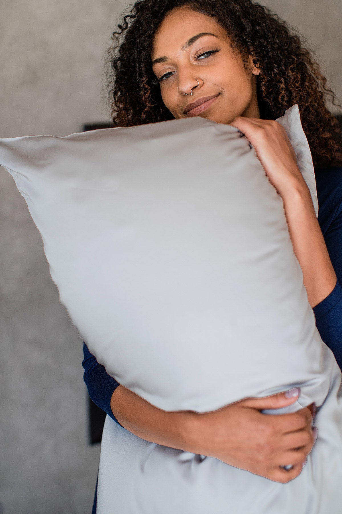 A woman with both arms wrapped around a pillow covered in a Yala Bamboo Dreams Luxe Sateen Pillowcase in Dove Grey