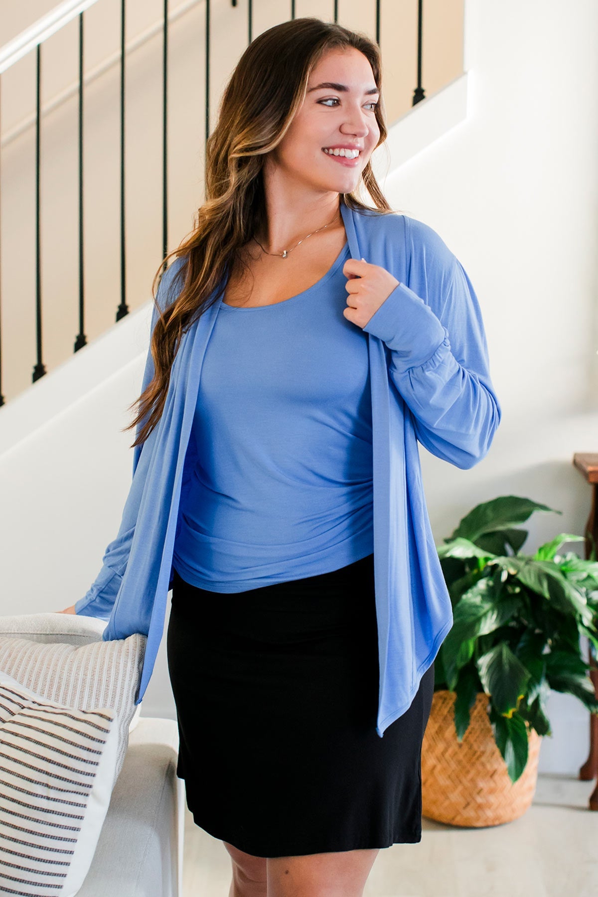 A woman standing and smiling while looking off to the side, wearing Yala Everly Puffed Sleeve Bamboo Wrap in French Blue