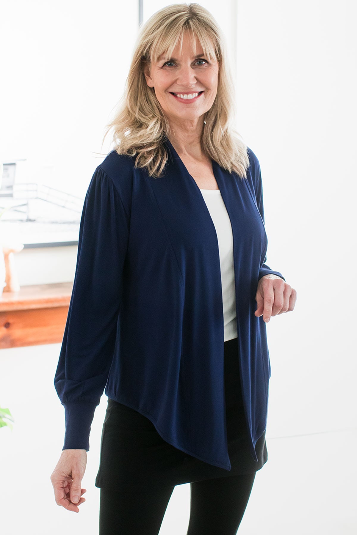 A woman standing and smiling with one hand raised to her sternum, wearing Yala Everly Puffed Sleeve Bamboo Wrap in Navy