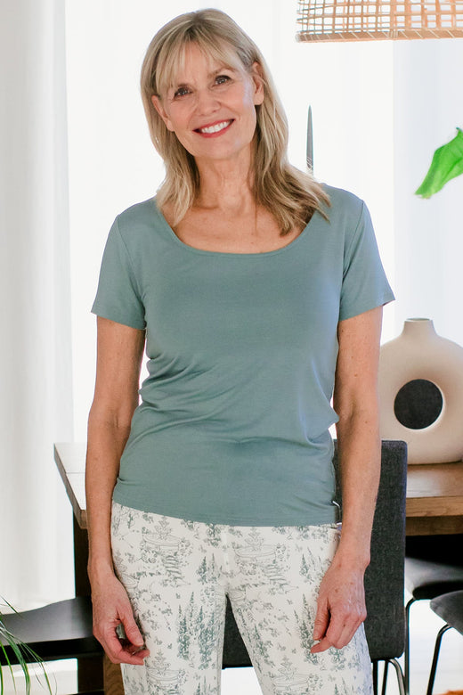 A woman standing and smiling with both hands at her sides, wearing Yala Heidi Scoop Neck Bamboo Tee Shirt in Matcha