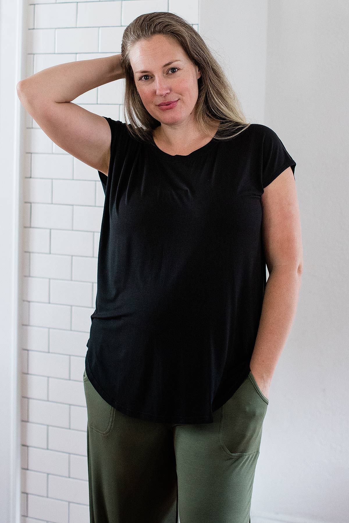 A woman standing and brusing her hair back with one hand, wearing Yala Cassidy Cap Sleeve Bamboo Boyfriend Tunic in Black