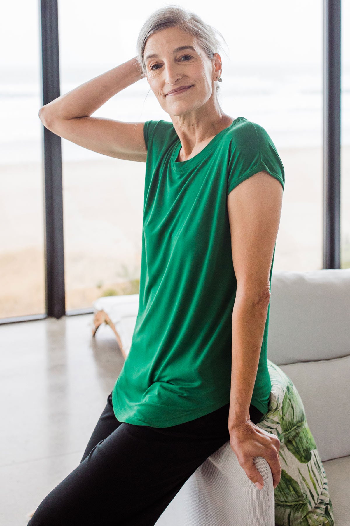 Woman sitting on the arm of a couch, one hand behind her head, wearing Yala Cassidy Cap Sleeve Bamboo Boyfriend Tunic