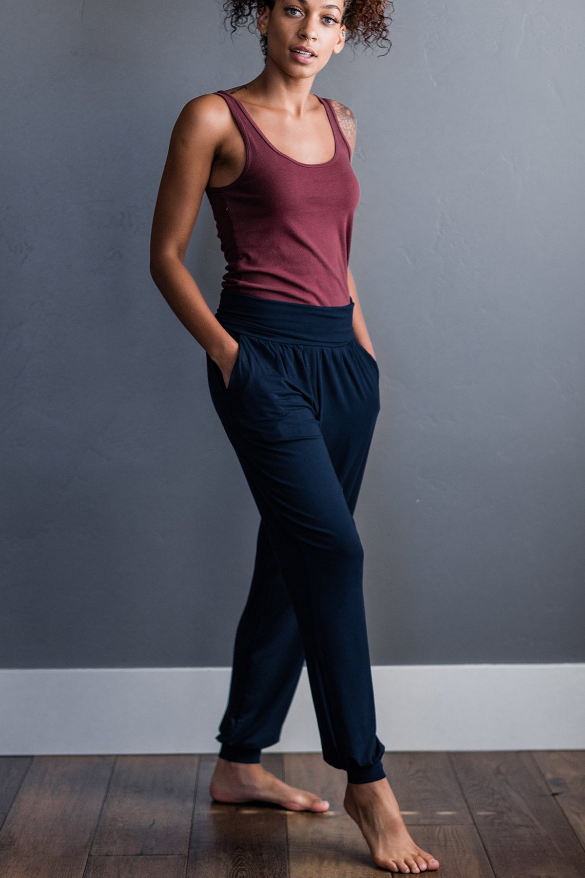 A woman standing facing slightly to the side with one foot outstretched and both hands in her pockets, wearing Yala Geena Lightweight Bamboo Jogger Lounge Pants in Navy