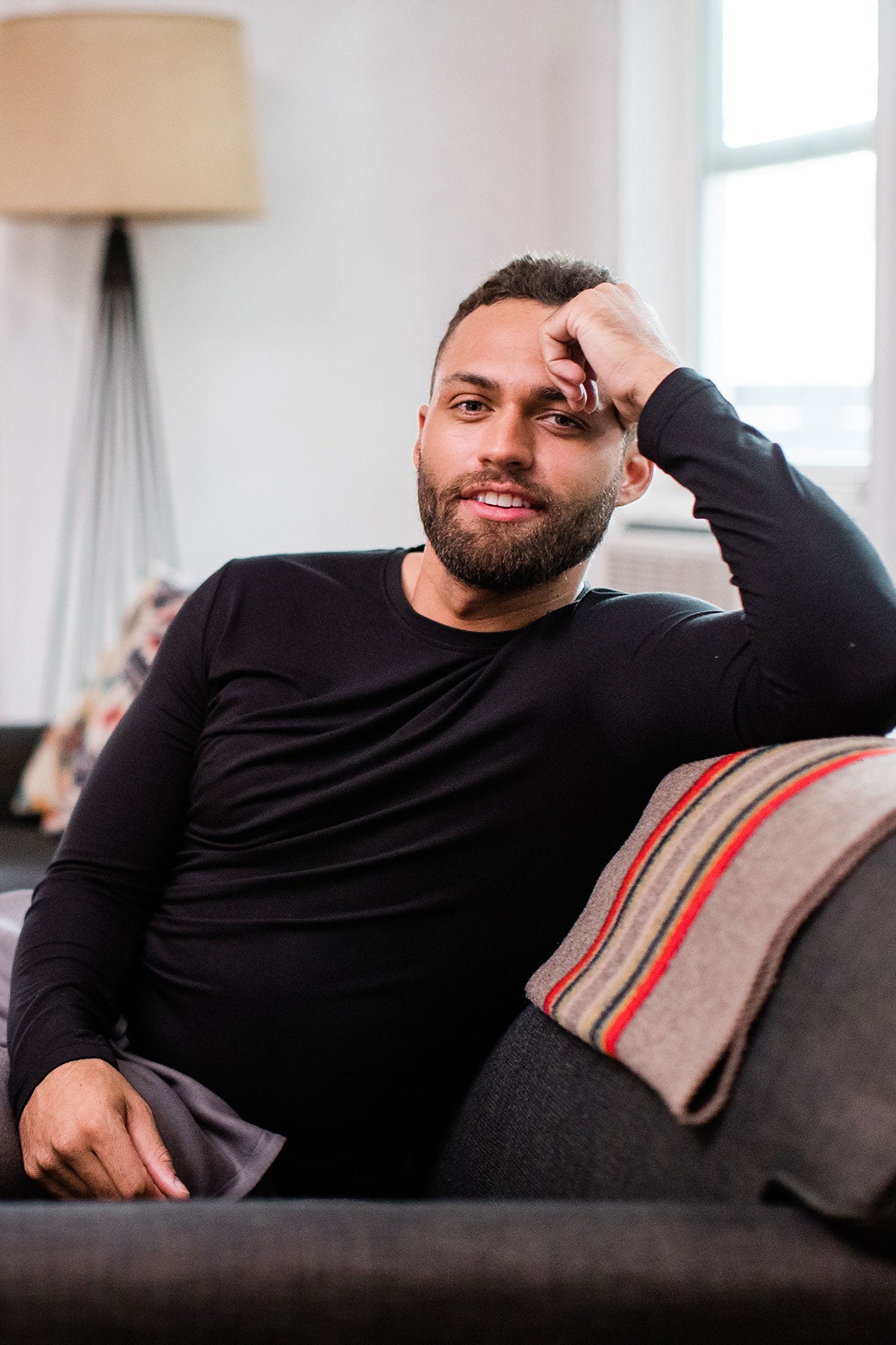 A man sitting on a couch with one hand raised to his head, wearing Yala Jonah Men's Long Sleeve Bamboo Crew Tee Shirt in Black