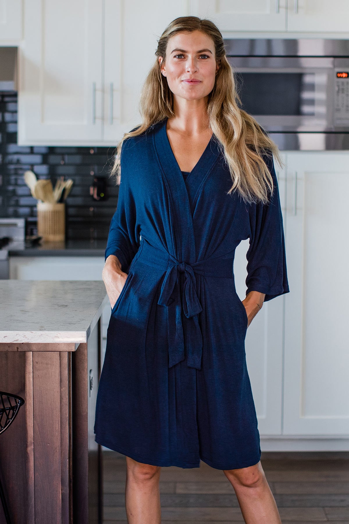 A woman standing and smiling with both hands in her pockets, wearing Yala Kendra Kimono Bamboo Sweater Robe in Navy