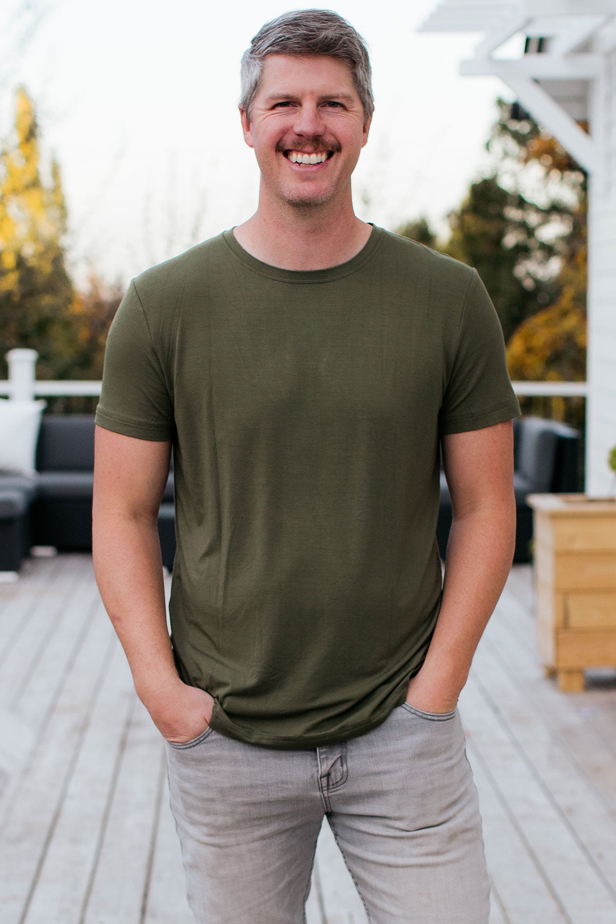 A man standing and smiling with both hands in his pockets, wearing Yala Nathan Men's Short Sleeve Bamboo Crew Tee Shirt in Moss