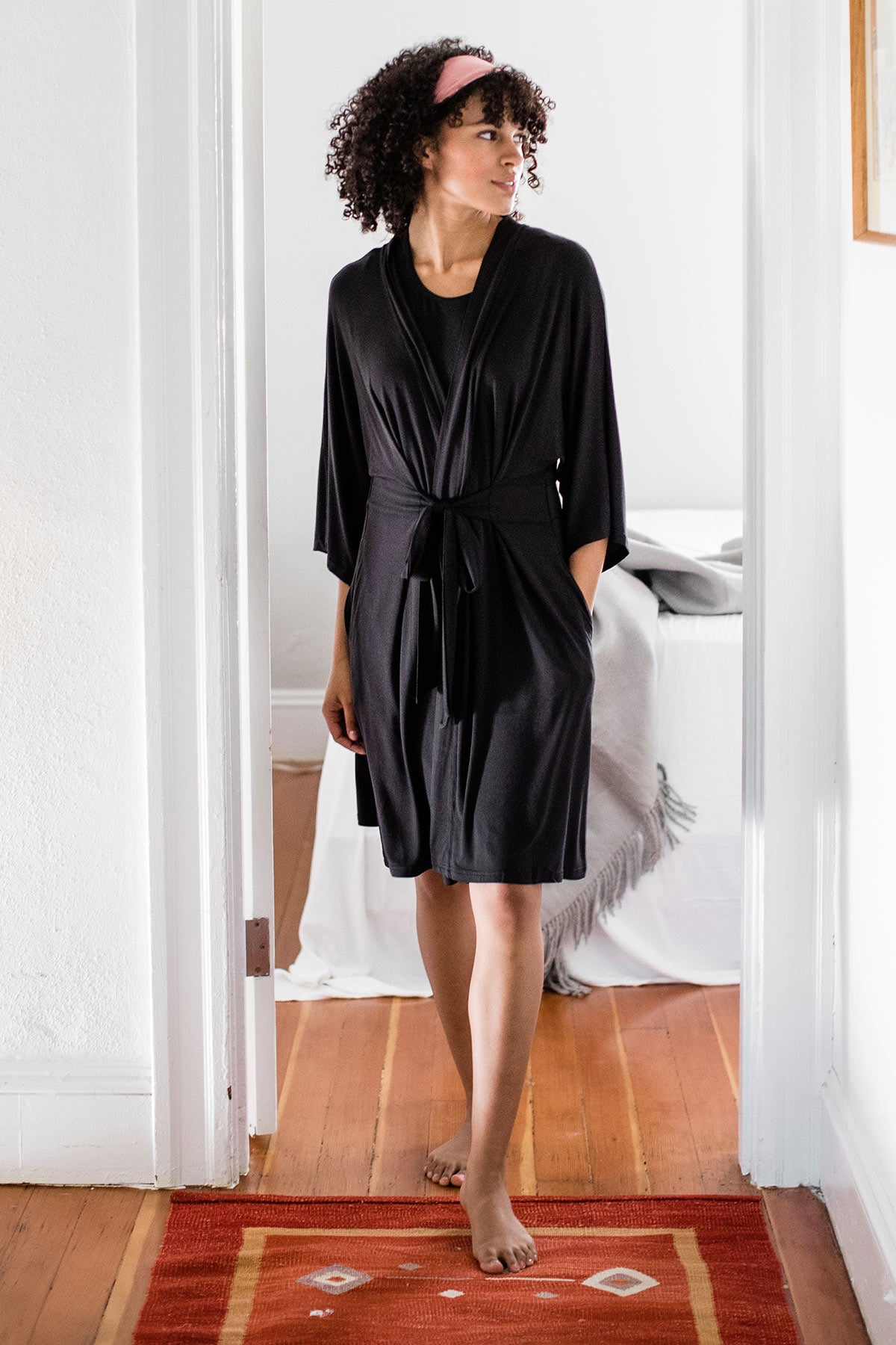 A woman walking forward with one hand in her pocket, wearing Yala Nina Elbow Sleeve Belted Bamboo Robe in Black