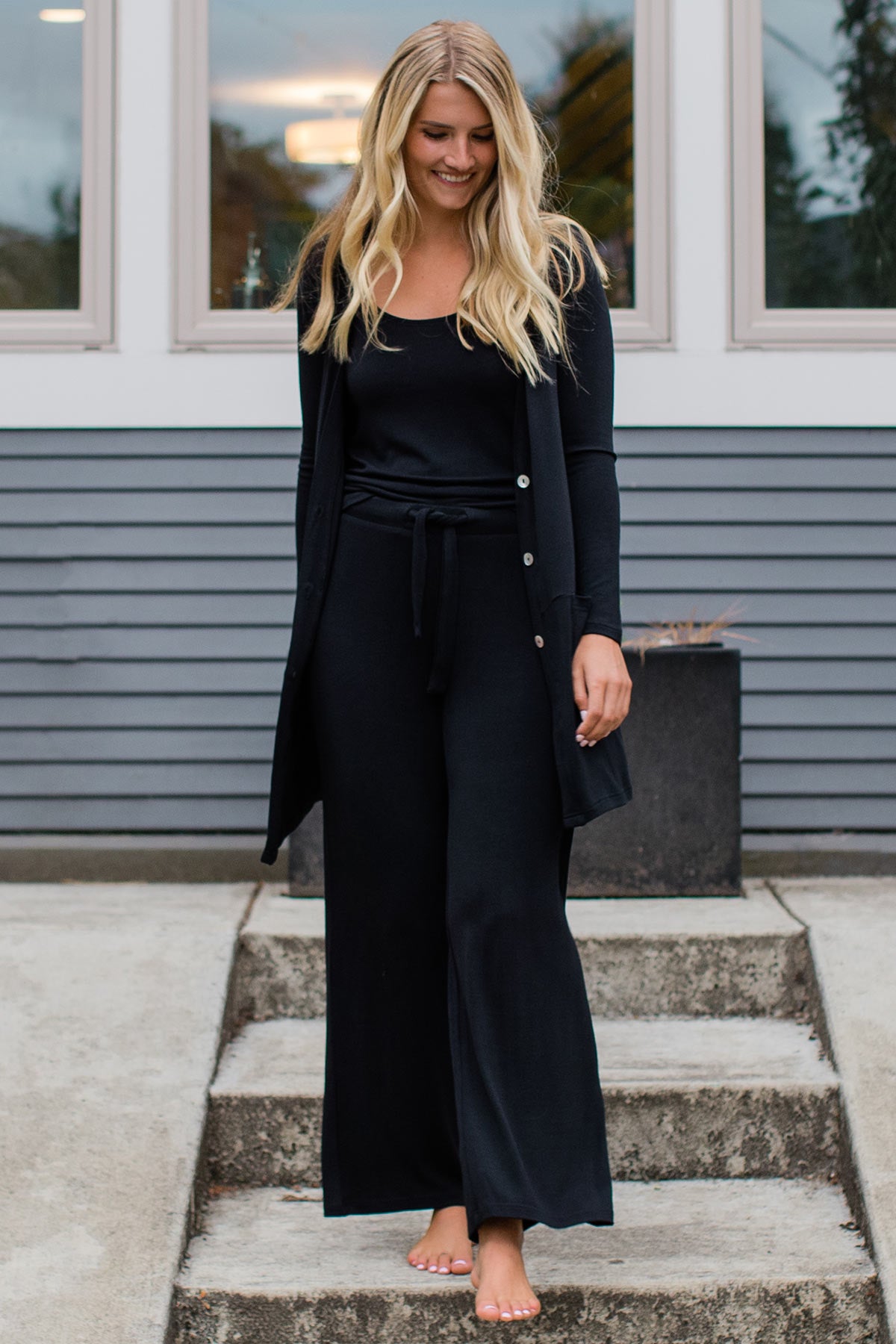 A woman walking down stone steps and smiling while looking down, wearing Yala Peyton Bamboo Sweater Drawstring Lounge Pants in Black