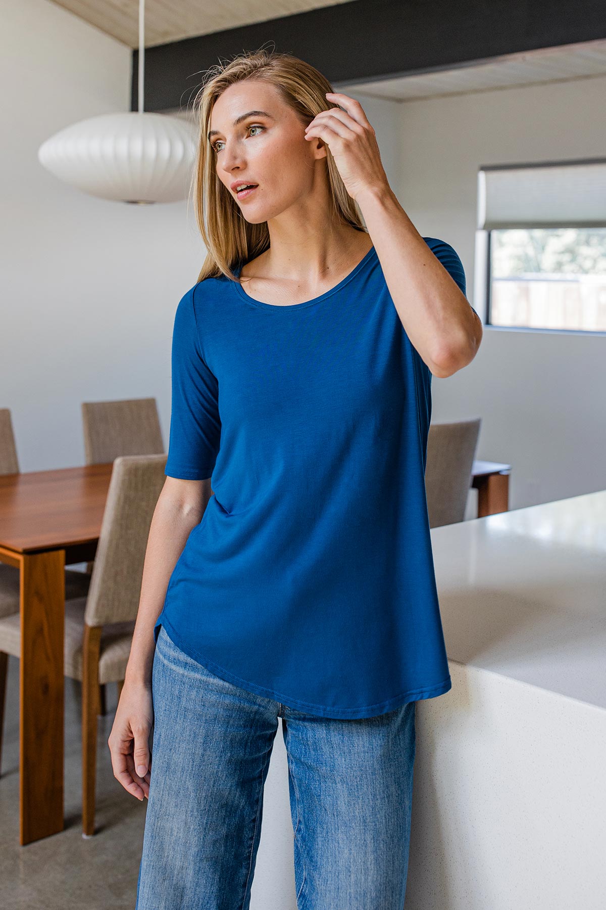A womand standing and brusing her hair aside with one hand, wearing Yala Sandy Relaxed Fit Scoop Neck Short Sleeve Bamboo Top in Lapis