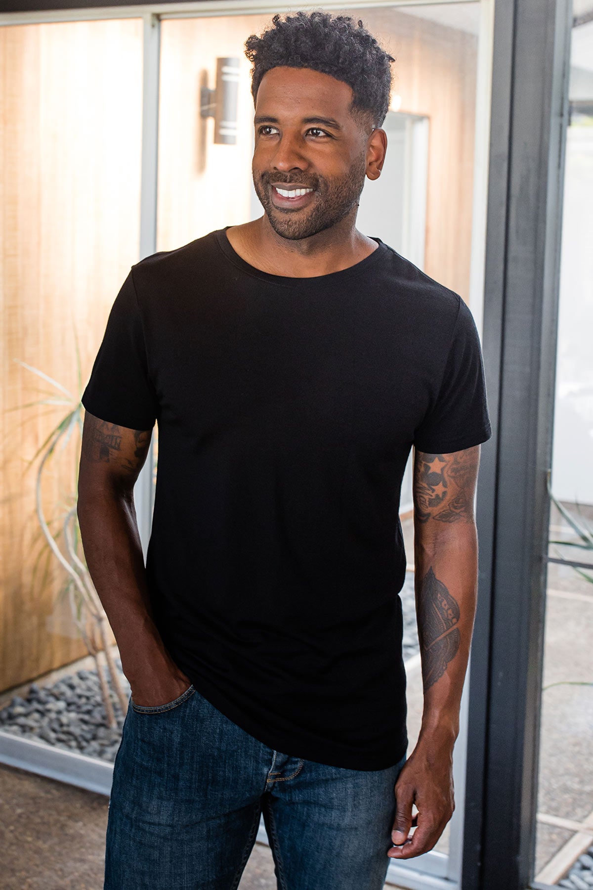 A man standing with one hand in his pocket, looking to the side and wearing Yala Superfine Merino Wool Short Sleeve Tee in Black