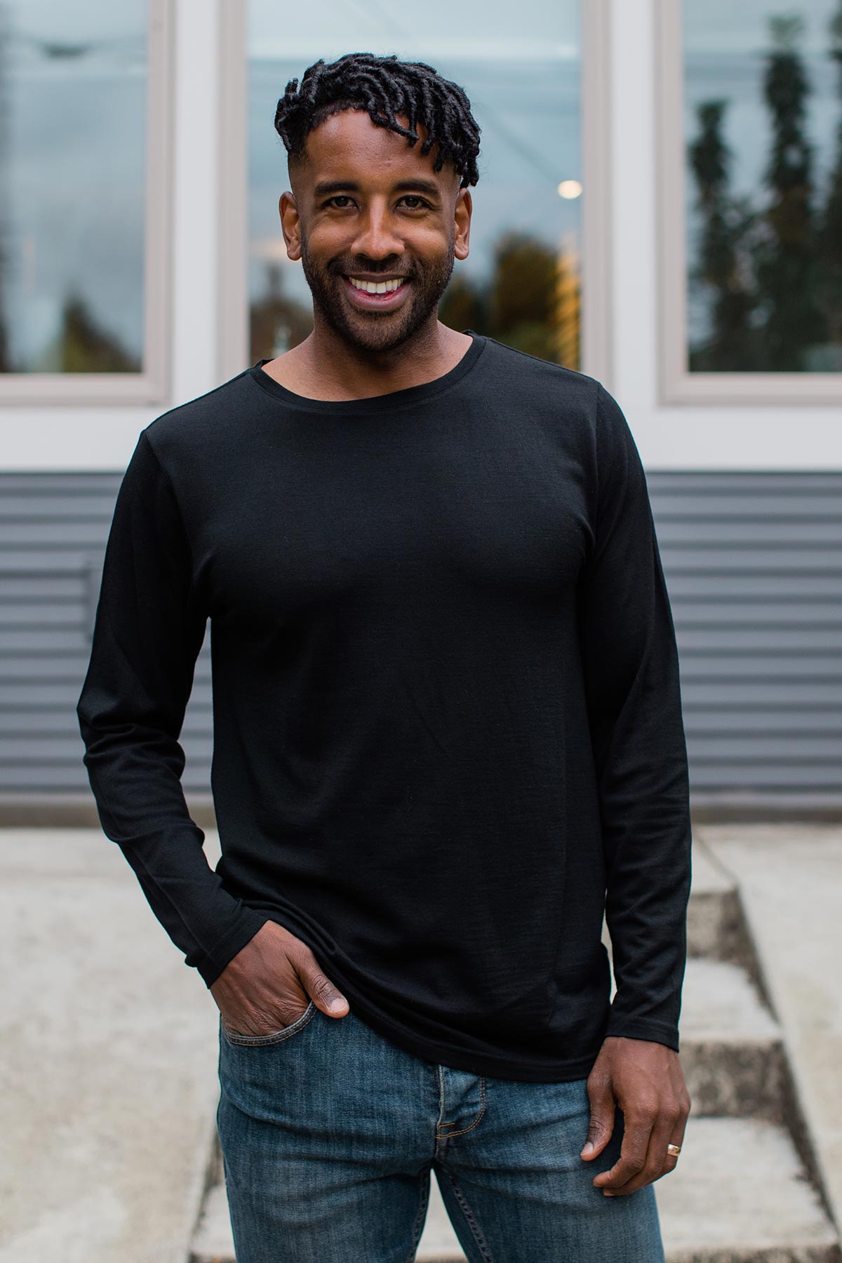 A man standing and smiling with one hand in his pocket, wearing Yala Superfine Merino Wool Long Sleeve Top in Black