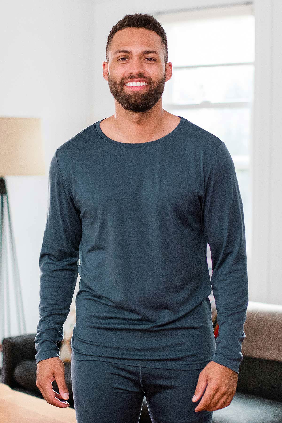 A man standing and smiling with both hands at his sides, wearing Yala Superfine Merino Wool Long Sleeve Top in Storm Grey