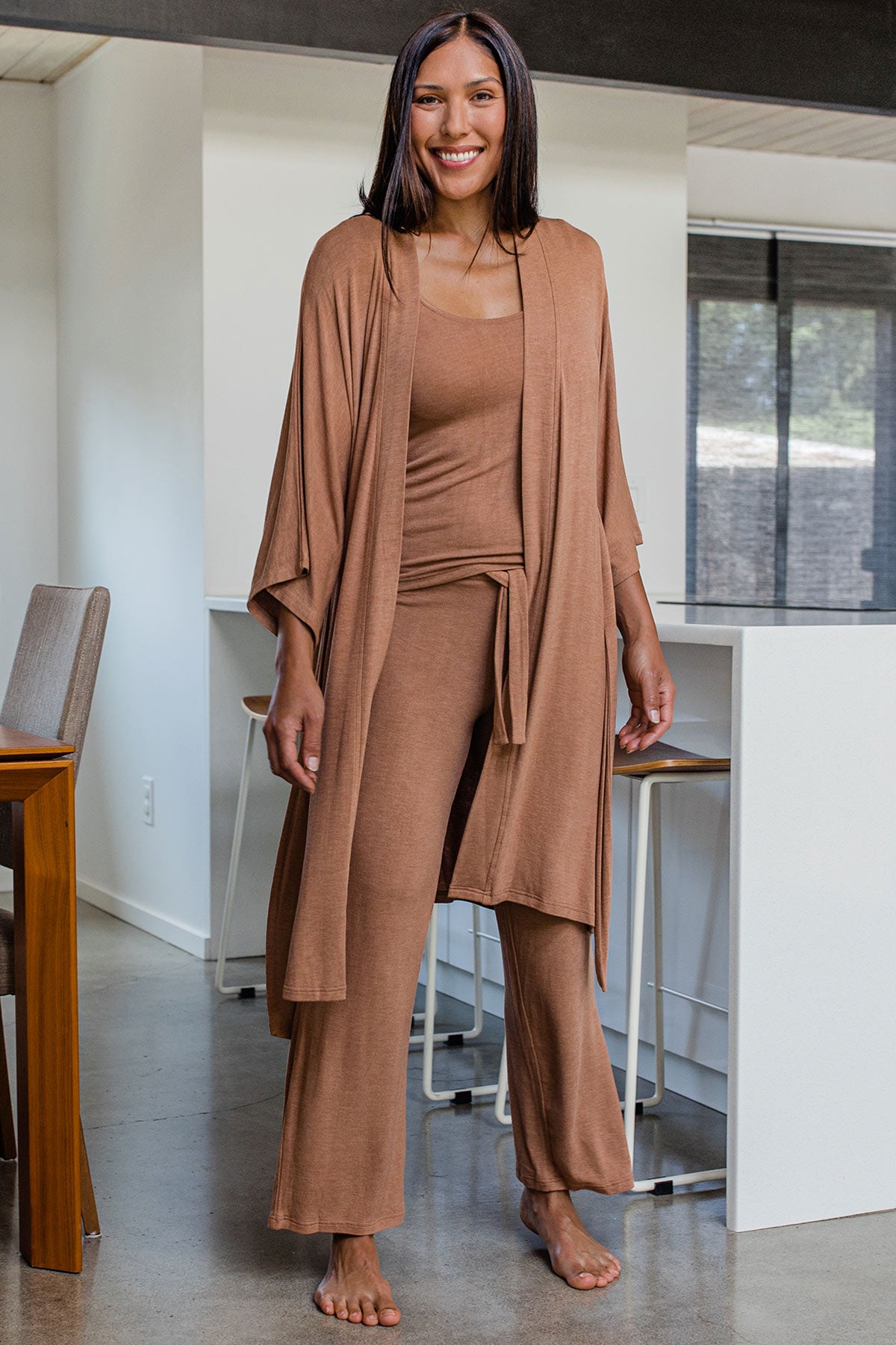 A woman standing and smiling, wearing Yala Kendra Kimono Bamboo Sweater Robe in Camel