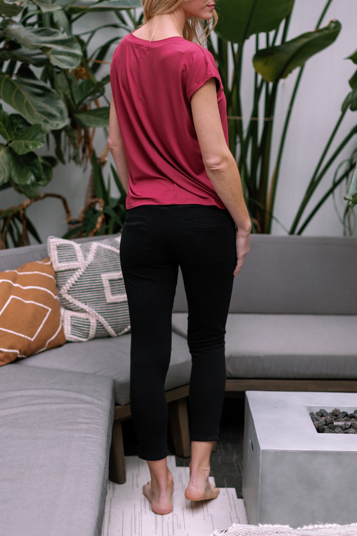 A woman standing and facing away from the camera, wearing Yala Abby Mid-Waist Cropped Bamboo and Organic Cotton Pencil Pants in Black
