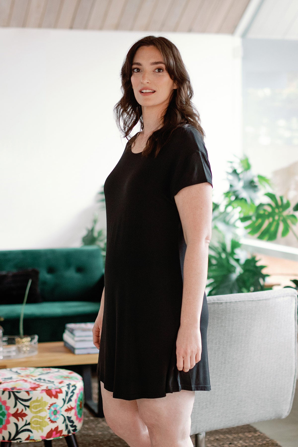 A woman standing turned to the side, looking towards the camera, wearing Yala Penelope Cap Sleeve Oversized Bamboo Nightshirt in Black
